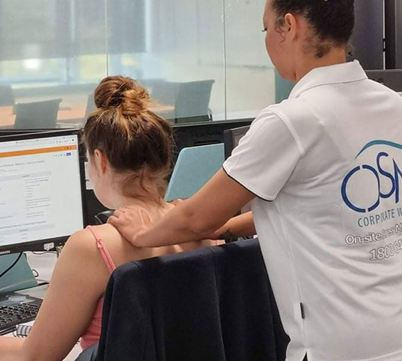 Office worker receiving a seated neck and shoulder massage from an on-site corporate massage therapist during work hours.